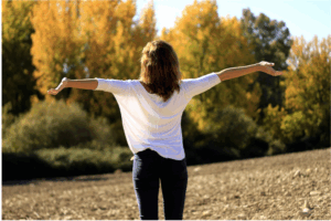 Woman standing outdoors with arms open toward the sun, symbolizing natural Vitamin D absorption through sunlight exposure — supports wellness and immunity.