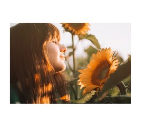 A woman basking in the sunlight, admiring a sunflower, representing a moment of mindfulness and connection with nature, as highlighted in 'The Power of Mindfulness' article.