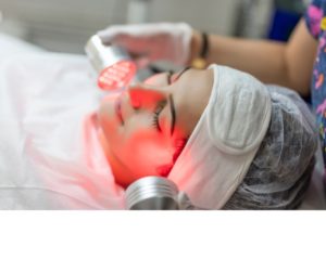 A woman receiving red light therapy on her face, with the light focused on her skin to showcase the treatment's targeted approach to enhancing facial health.