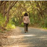 Healthy Stride: A woman walking along a scenic path, immersed in the tranquility of her surroundings, taking steps towards wellness and embodying an active lifestyle. 44 Simple Health Hacks.