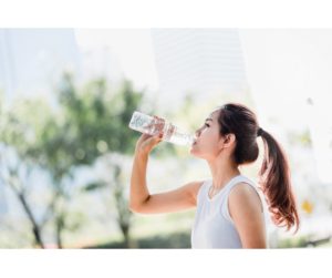 Image of a woman drinking water from a clear glass, showcasing the importance of hydration. She appears refreshed and healthy, emphasizing the benefits of staying hydrated for overall well-being