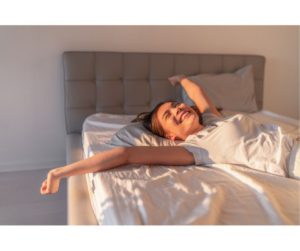 A woman waking up refreshed and energized after a good night's sleep, her expression peaceful and content, with morning light casting a soft glow around the room, highlighting a sense of new beginnings and the rejuvenating power of rest.