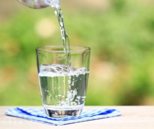 A clear glass of water with a vibrant splash, set against a serene blue background, symbolizing hydration as the key to maintaining youth and health. Slowing Down Aging. 