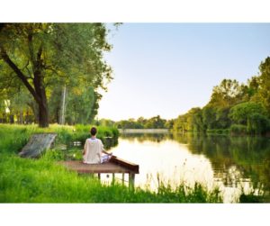 A tranquil and calming image of a person meditating in a serene setting, surrounded by elements of nature like a serene lake, lush greenery, or a gentle sunrise. The individual is in a classic meditation pose, exuding deep peace and mindfulness. The setting and the person's composed demeanor symbolize the essence of mindfulness and the importance of mental wellness, creating an atmosphere of tranquility and introspection.