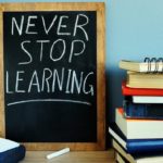 Books and a chalkboard with 'Never Stop Learning' written on it, symbolizing the continuous journey of education and personal growth. Simple Habits for Happiness.