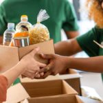 An image of someone generously handing a box of groceries, illustrating the act of giving back and supporting others in need. Simple Habits for Happiness.