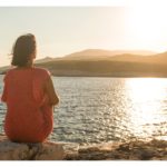 A woman gazing thoughtfully at the water, symbolizing the practice of reflection and adjustment for personal growth and resilience. Simple Habits for Happiness.