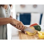 A woman meal prepping, cutting a pepper to prepare healthy meals efficiently.