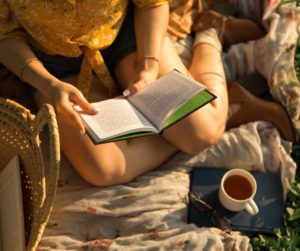 Mom relaxing reading a box and enjoying a coffee outside on a beautiful sunny day. Time Hacks for busy Moms.