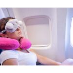 A woman using a neck pillow and eye mask on a plane, highlighting tips for creating a calm travel environment to stay healthy and mindful while traveling.