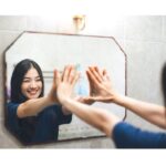 A woman smiling at her reflection in the mirror, expressing self-love and confidence.