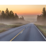 Morning mist blankets the horizon over a quiet highway, capturing the tranquil essence of a fall daybreak.