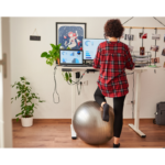 A woman sitting on an exercise ball at her desk, transforming her home office for better wellness and posture.