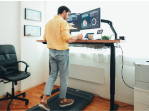 A man using a compact walking elliptical under his desk, promoting movement and wellness while transforming his home office.