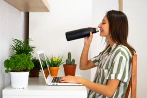 A woman sitting at her desk, taking a sip from a smart water bottle, transforming her home office into a wellness-focused space.