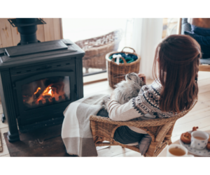 A woman relaxes by a cozy fire, her cat curled up beside her. The warm glow and peaceful ambiance help soothe her mind, improving her sleep and mental health.