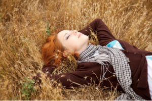 A woman lying in a golden field, relaxed and serene, illustrating the stress-relieving benefits of nature and the outdoors.