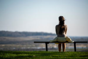 A woman sitting on a bench overlooking a vast landscape, enjoying the calming benefits of nature and peaceful solitude.