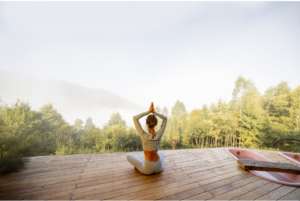 Woman meditating in a lotus position on a wooden deck overlooking a misty forest at sunrise, embodying tranquility and mindfulness. Real Self-Help for Everyday Life!