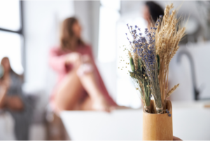 Relaxed setting in a bright bathroom with a person soaking in a bathtub, surrounded by natural elements like lavender and wheat, evoking a sense of calm and self-care.