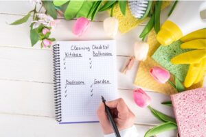 A spring cleaning checklist on a notebook surrounded by cleaning supplies and spring flowers, emphasizing organized and refreshed living spaces.