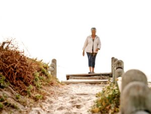 A mature woman walks confidently along a wooden path to the beach, symbolizing fresh starts and personal growth.Spring Cleaning Mind and Space.