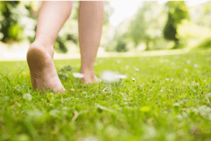 A close-up of a person’s bare feet walking slowly on lush green grass, symbolizing grounding and a connection to nature. Simple summer habits. 