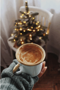 A warm holiday latte in front of a small Christmas tree, capturing the cozy seasonal atmosphere linked to stress and the body connection.