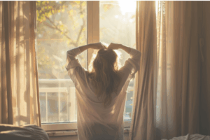 A woman stretching by a bright window, showing gentle morning practices that support stress and the body connection.