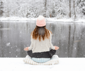 A woman meditating beside a snowy lake, illustrating mindful ways to support stress and the body connection.